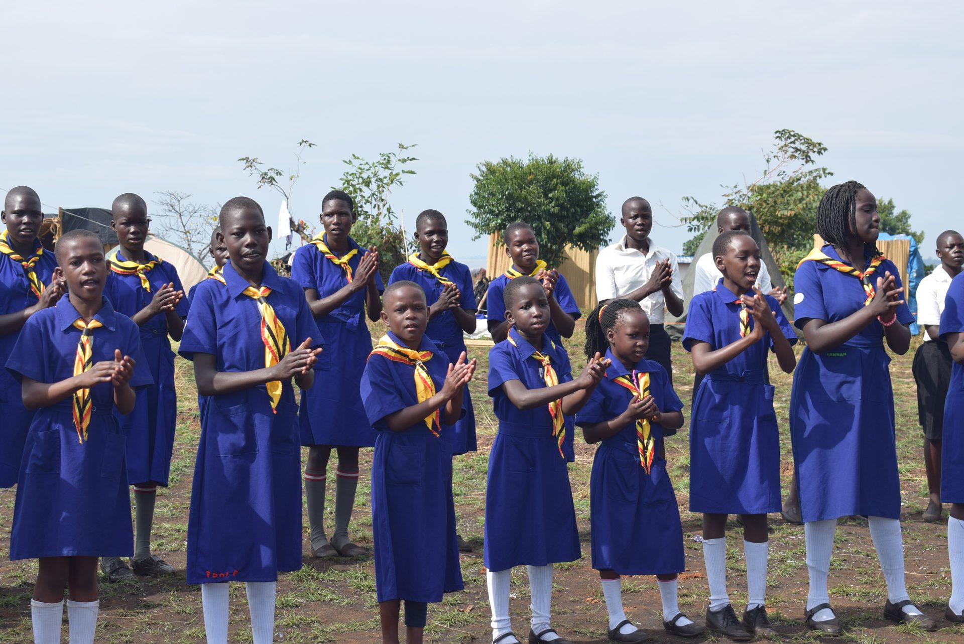 Girl Guides in blue uniform singing together at a lakeside campsite